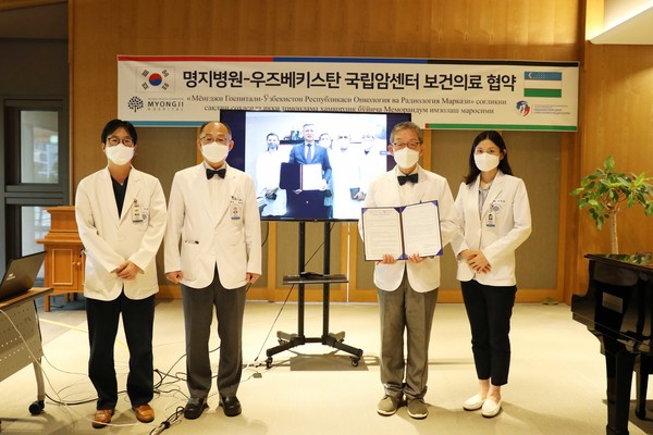 Myongji Hospital Director-General Kim Sae-chul (second from right) and Tillyashaikhov Mirzagaleb Nigmatovich (on the screen to Kim’s left), director of the Republican Specialized Scientific-Practical Medical Center of Oncology and Radiology of Uzbekistan, hold up their cooperative agreement on Wednesday.