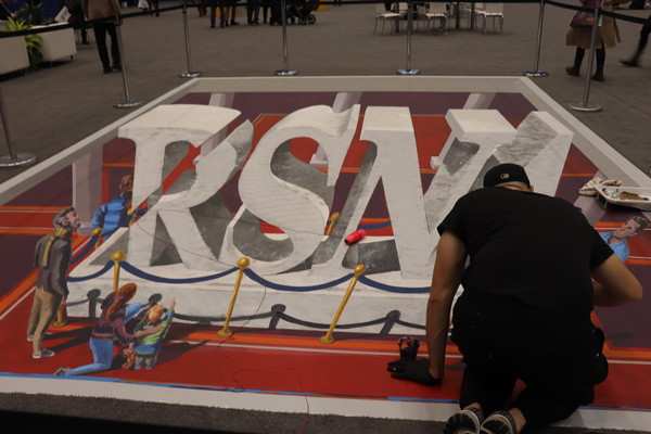 An artist painting a 3D painting of the RSNA logo on the ground.