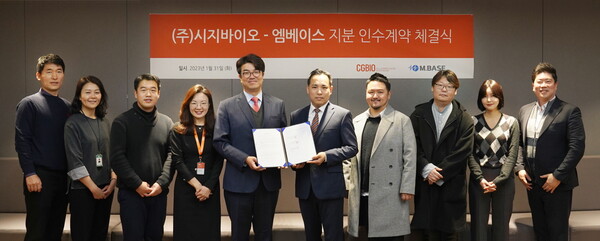 CG Bio CEO Yu Hyun-seung (fifth from left) and M.Base CEO Yoo Jin-ho (to Yu’s right) hold up the acquisition agreement at CG Bio headquarters in Yongsan-gu, Seoul, Thursday.
